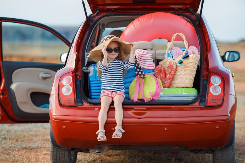 Little girl in straw hat sitting in the trunk of a car | Mit Kind und Kegel in die Ferien