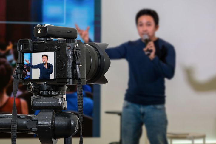 Professional digital Mirrorless camera with microphone on the tripod recording video blog of asian Speaker on the stage seminar, Camera for photographer or Video and Technology Live Streaming concept | Die zukunft ist digital und online