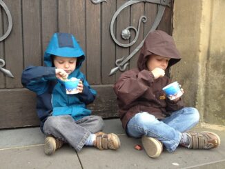 Kinder sitzen vor einem Tor und löffeln Eis