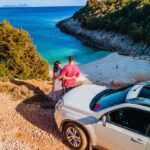 Pärchen mit dem Mietwagen an der Küste