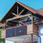 Frau putzt Solaranlage am Balkon eines Hauses