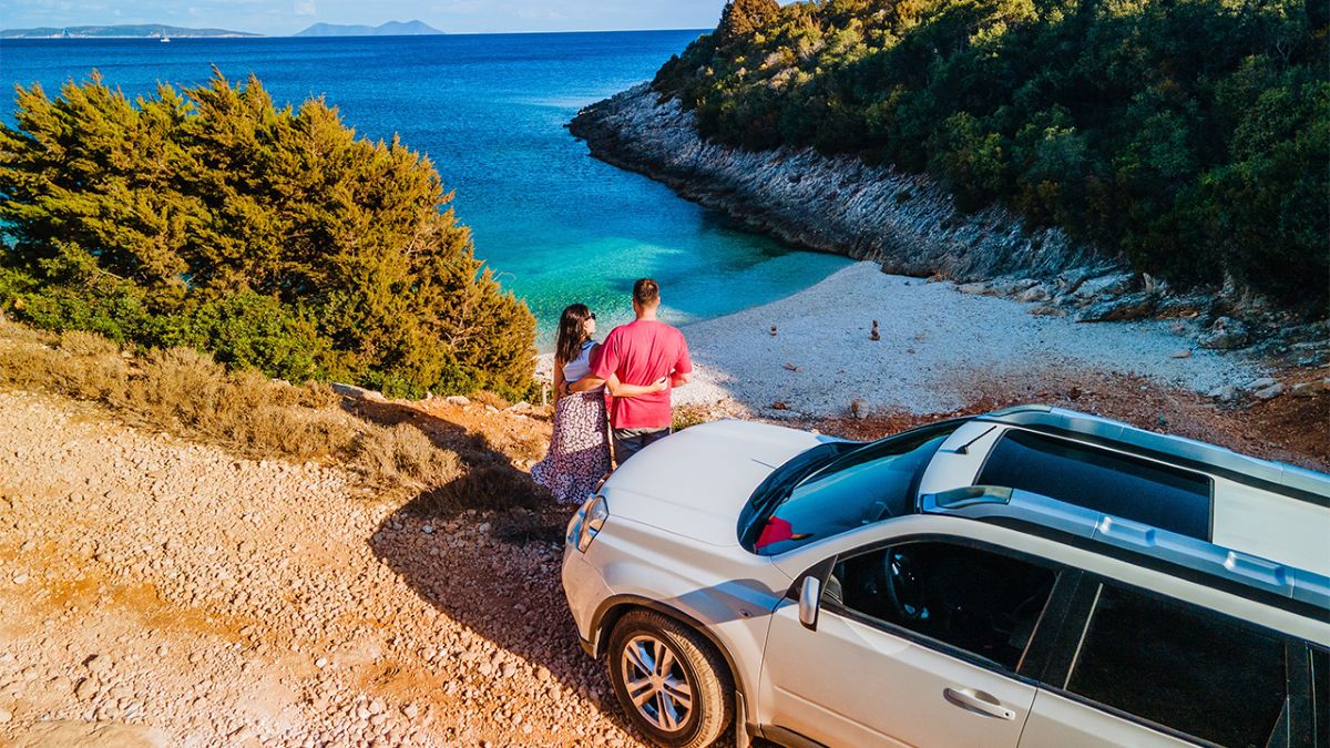 Pärchen mit dem Auto oberhalb einer Strandbucht | Pärchen mit dem Auto oberhalb einer Strandbucht