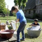 Kinder probieren beim Sommerspaß bäuerliches Leben im letzten Jahrhundert