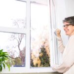 Frau macht im Herbst das Fenster weit auf