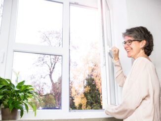 Frau macht im Herbst das Fenster weit auf