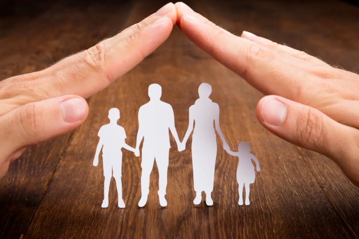 Hände über Scherenschnittfamilie bilden ein Dach