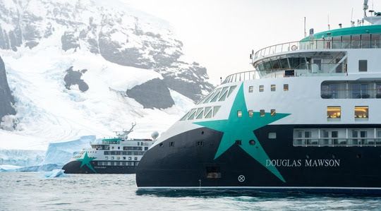 Expedition cruise ship in icy waters with snow-covered mountains; hull shows the name Douglas Mawson.