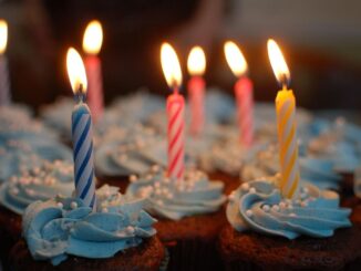 Cupcakes with blue frosting and striped birthday candles lit on top.