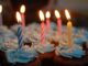 Cupcakes with blue frosting and striped birthday candles lit on top.
