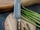 Chef's knife with a wooden handle rests on a round cutting board beside fresh asparagus spears.