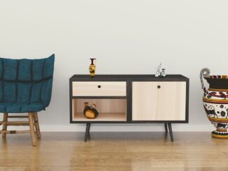 Blue tufted chair with wooden legs sits next to a two-door black-framed sideboard on a light wall.