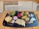 Cheese board on a black tray with assorted cheeses, grapes, and small bowls of cubes on a wooden table.