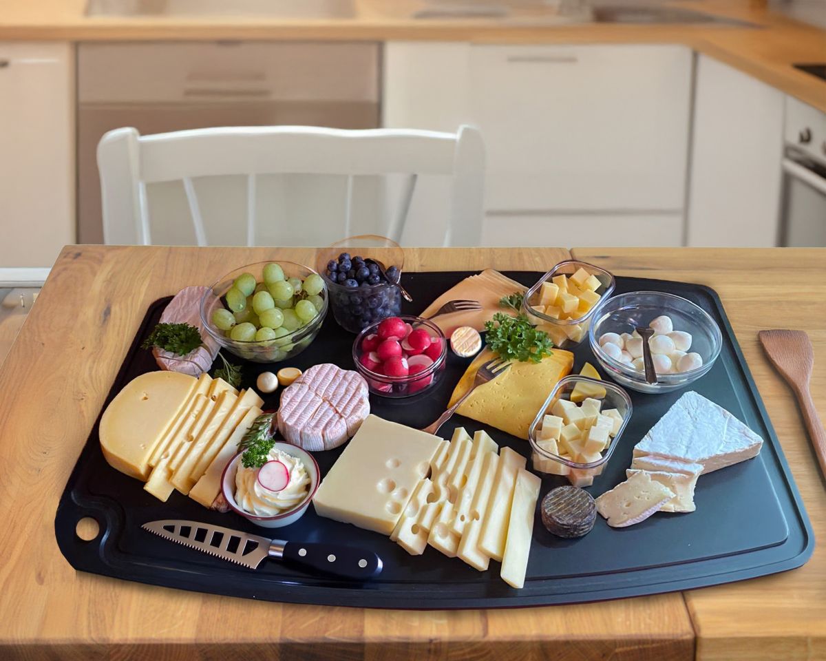 Cheese board on a black tray with assorted cheeses, grapes, and small bowls of cubes on a wooden table.