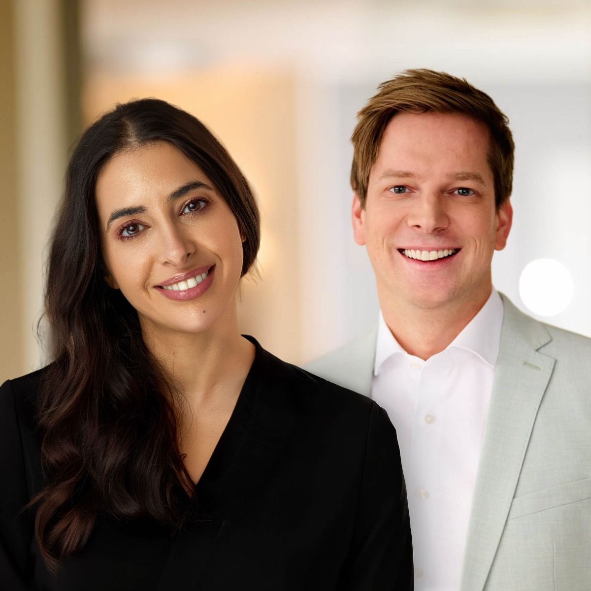 Two professionals, a woman in a black top and a man in a light suit, smiling for a team photo.