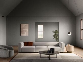 : Ein Sofa in der Mitte des Raums auf einem quadratischen Teppich, dazu Beistelltische und ein Sessel